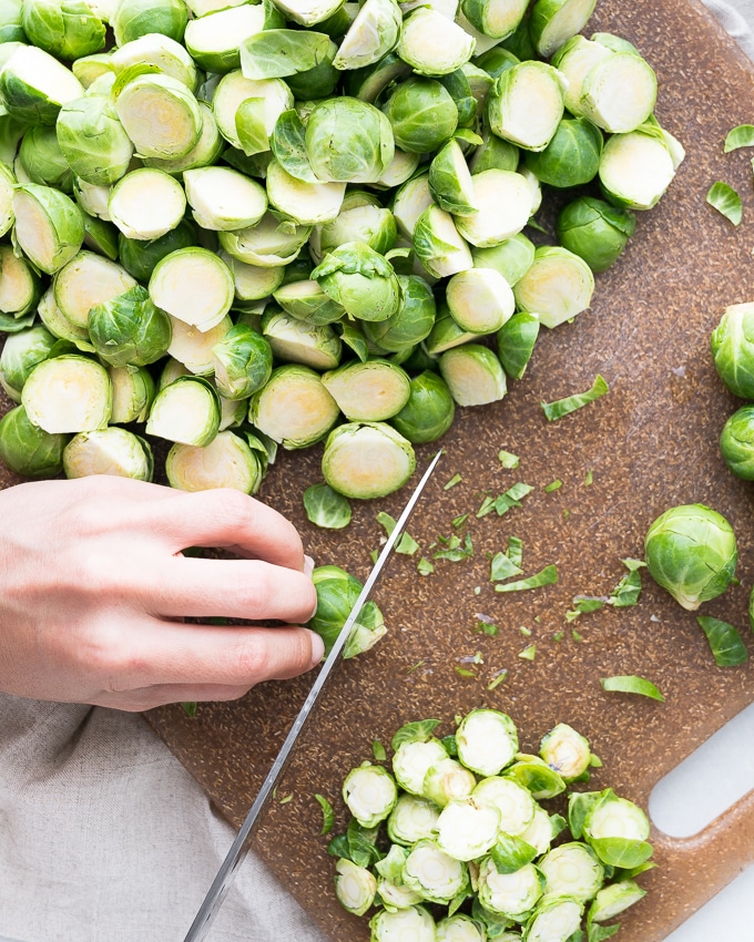 knife cutting Brussels sprouts on a brown cutting board